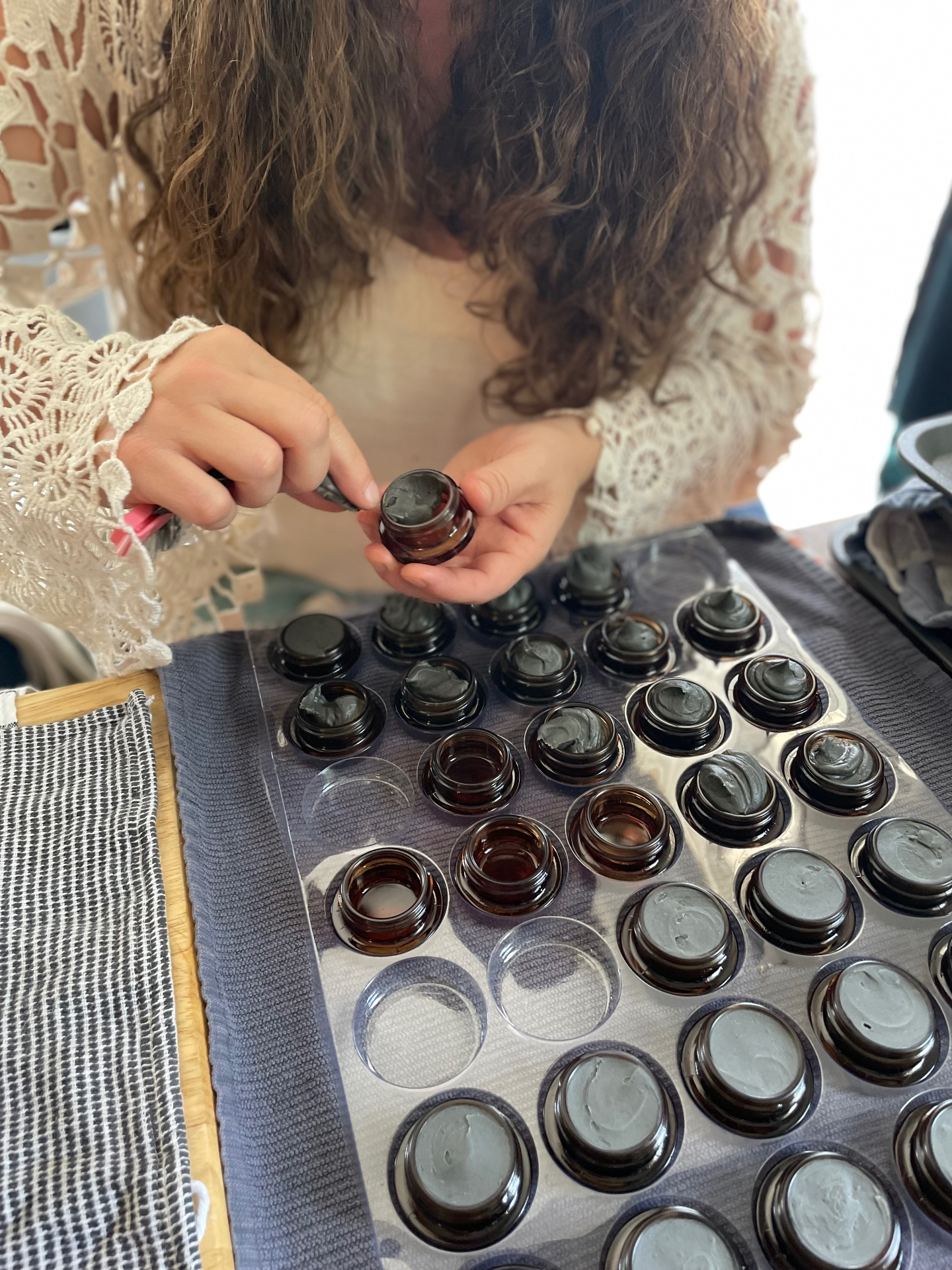 Bee filling amber glass jars with handmade clay skincare